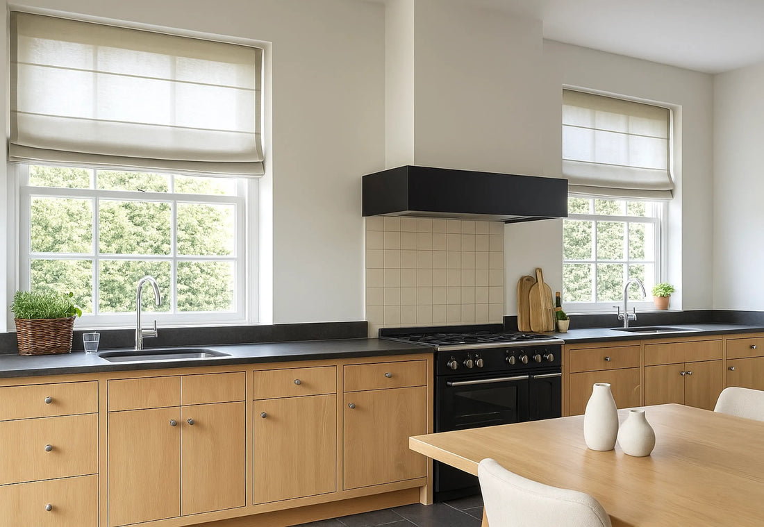 Modern kitchen remodel with light wood cabinets, black countertops, and linen Roman shades over two large windows.